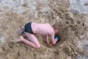 beach scene where a child is digging a hole in the sand.