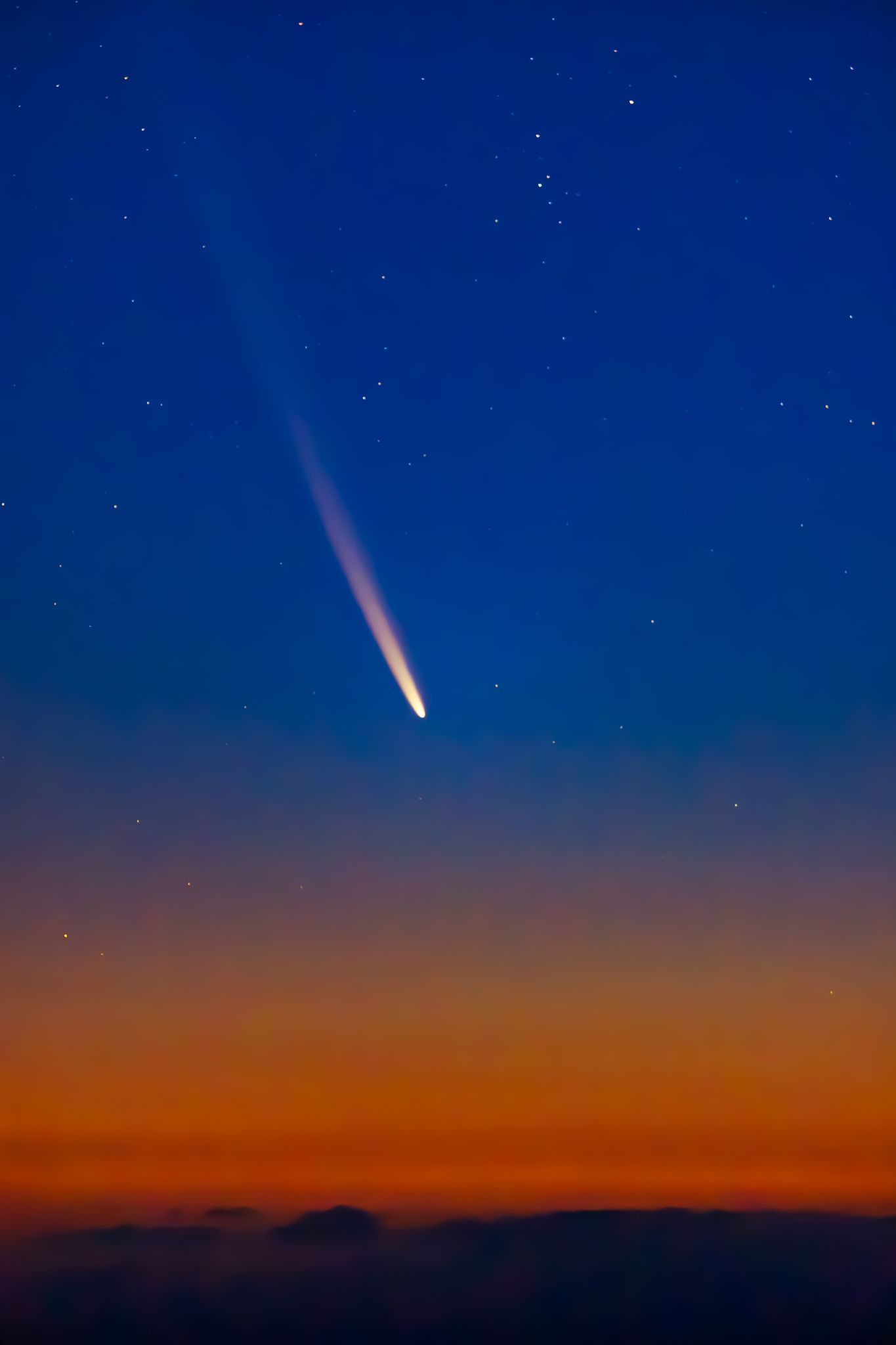 Orange to blue sky with dark horizon and a bright, white comet at center.