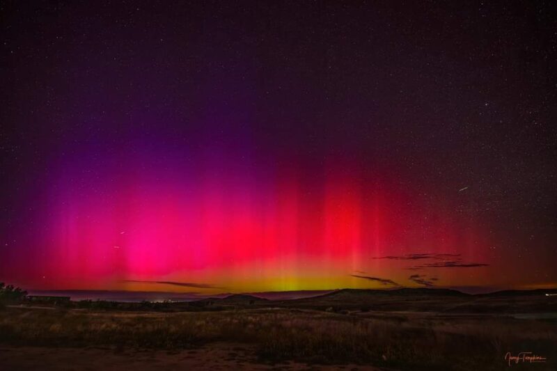 View with a yellow horizon that transforms into red, and then purple. There rest of the sky is dark, and has many stars. There are a few white, short streaks.