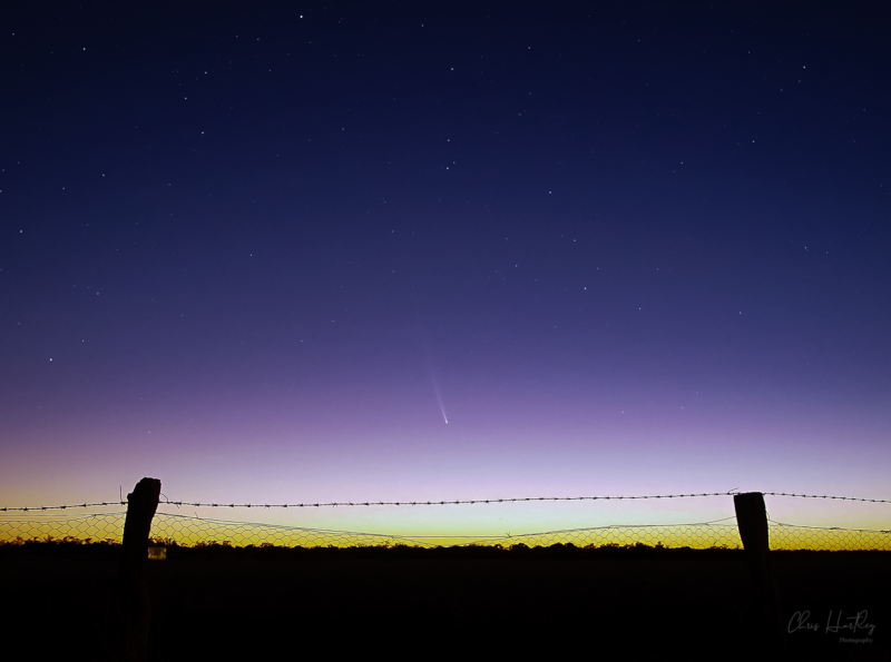 Fence at foreground with lightening sky and dim comet at center.