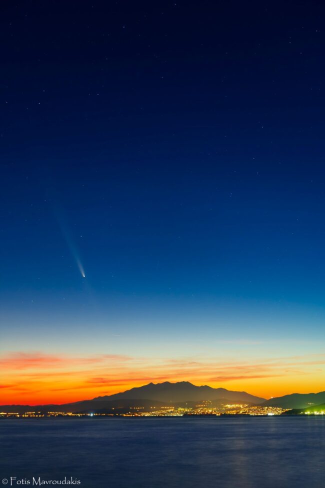 A hill and city lights with water, colorful sunset and the comet.