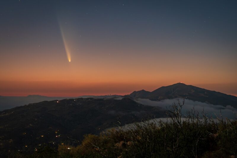 Sunset colors over the mountains with a comet that has a long tail.