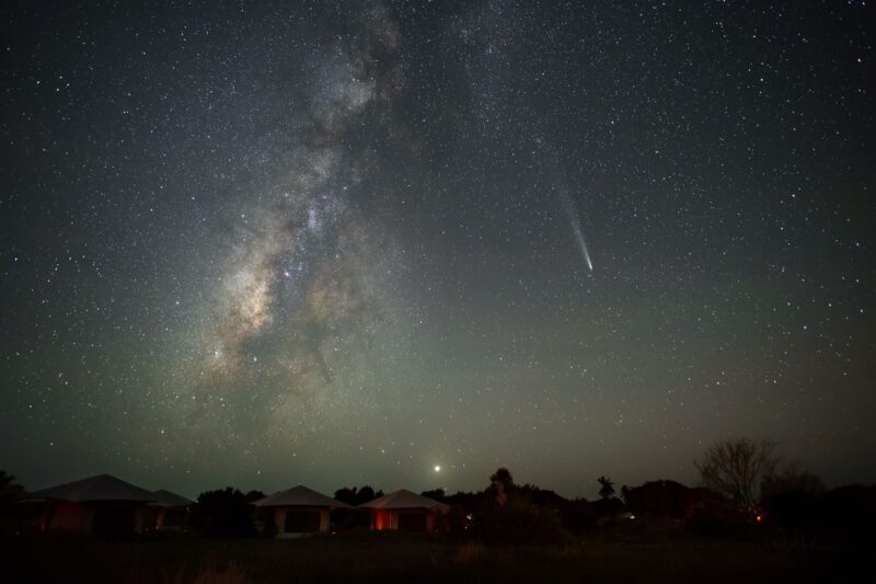 Night sky full of stars. There is a fuzzy object with a tail to the right side. There is a band of stars to its left.