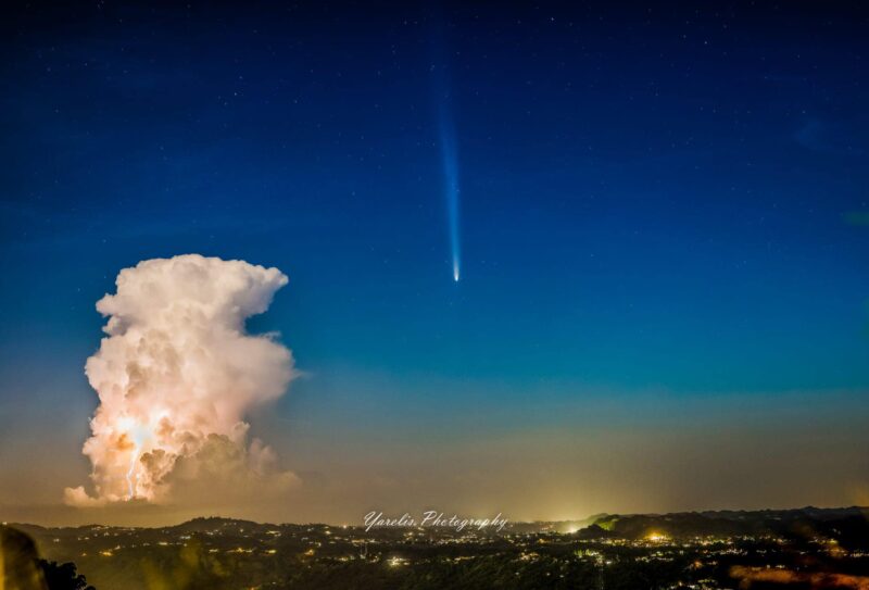 A comet over a city lit up, alongside a thunderstorm.