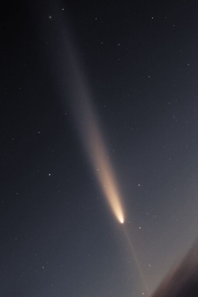 A bright comet with a fainter line extending from the head toward the ground.