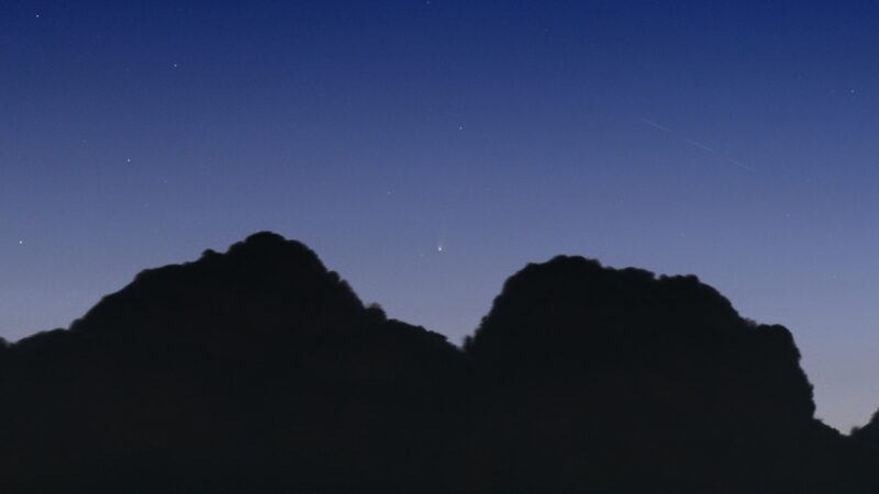 Two rocky projections with a comet above and between them in a somewhat dark sky.