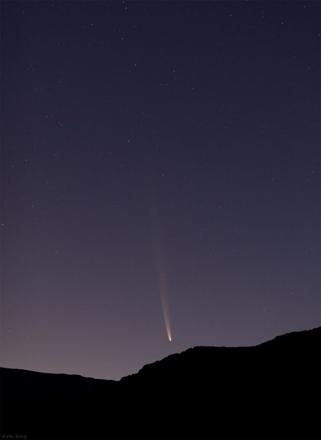 Sunrise sky with a comet over mountains.