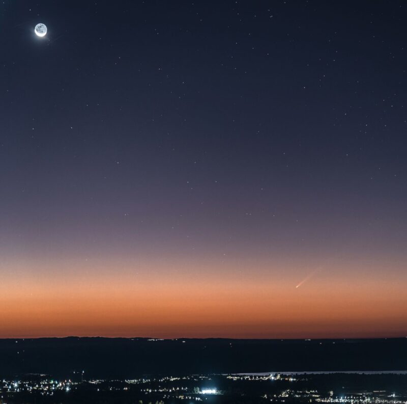 Lights of a city and sunrise with the moon and a comet.