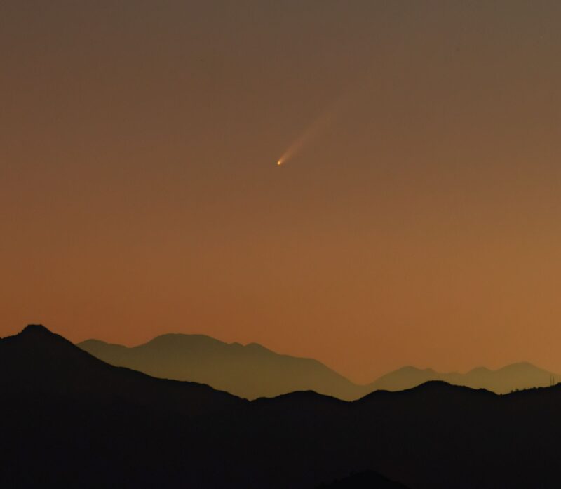 Tan-ish sky with a white comet and mountains.