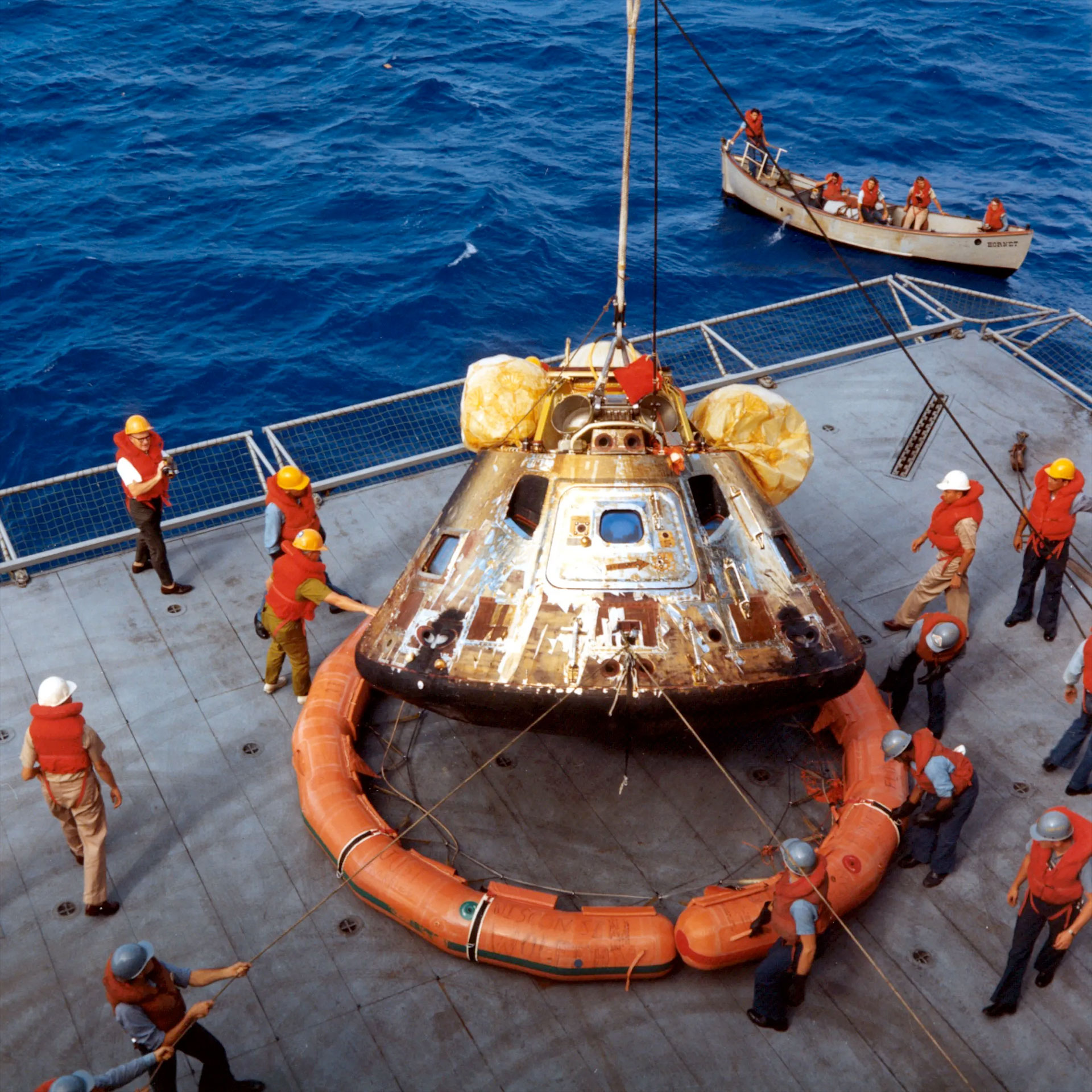 a space capsule is lifted by crane onto the deck of an aircraft carrier after splashing down from the moon.