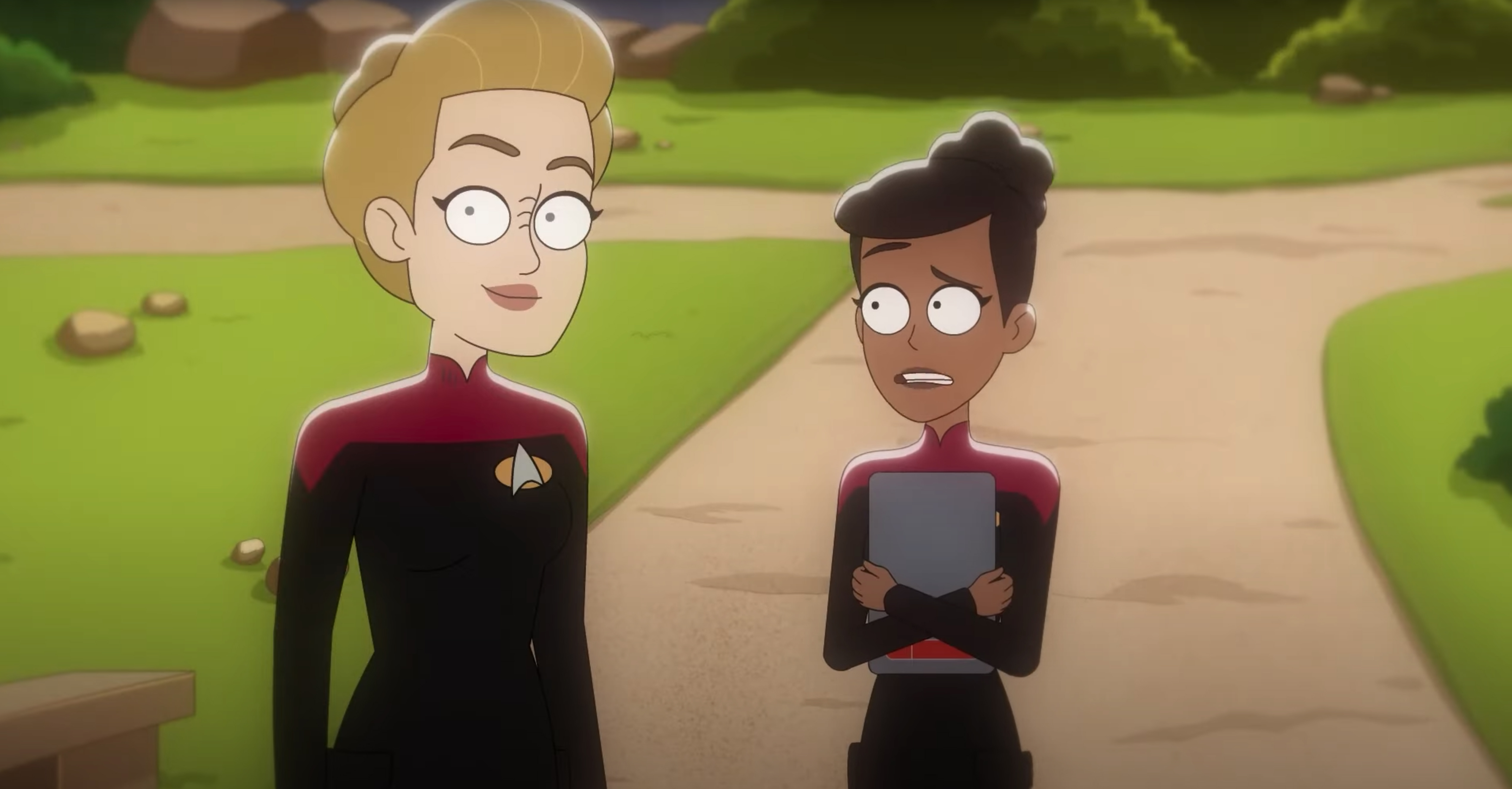 Two women in Starfleet uniforms, stood on a path in a garden area.