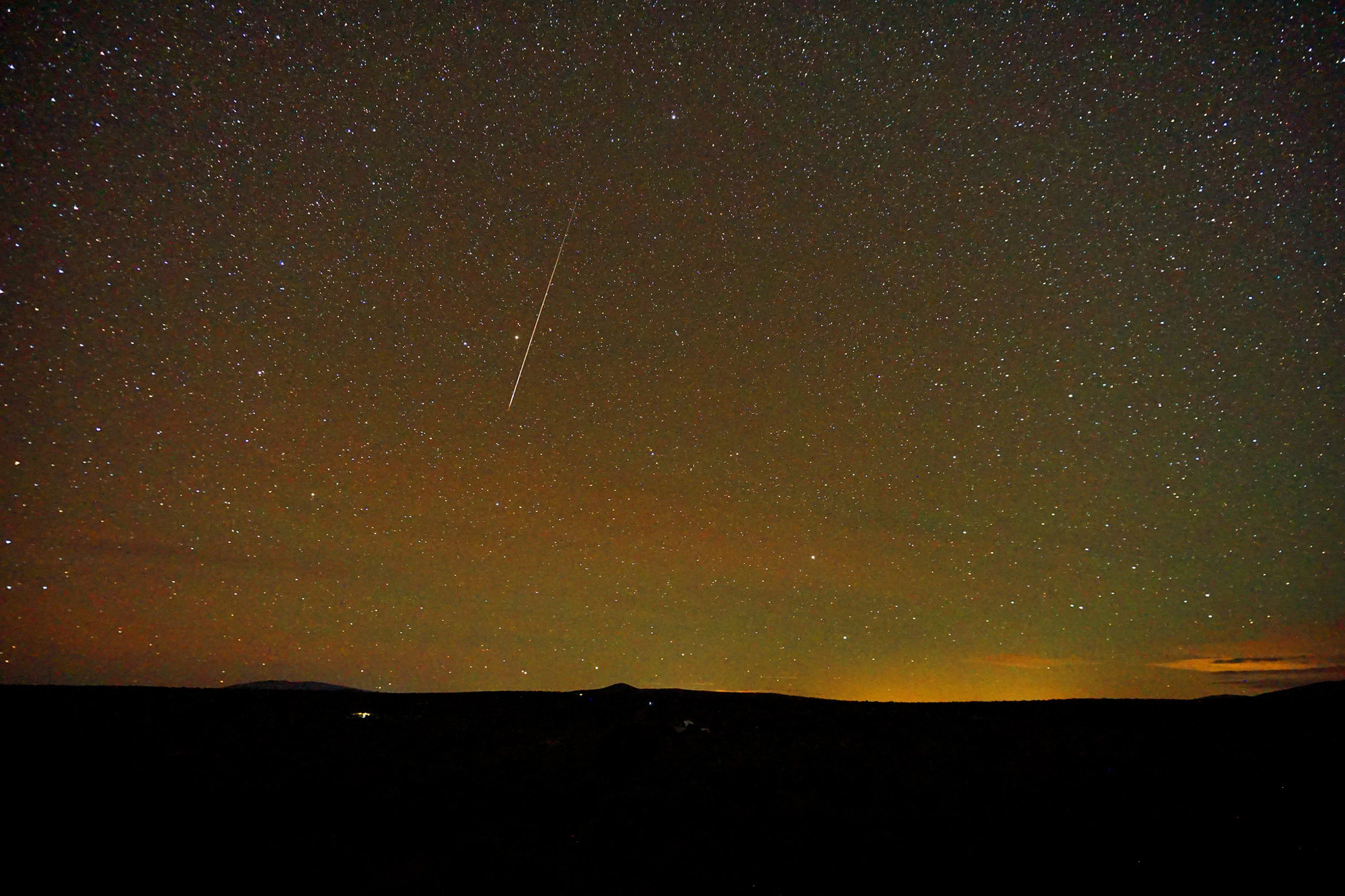 a long white streak of a meteor against a starry sky.