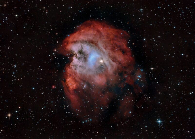 Large nebulous patch with bright red and blue swirls, dark lanes and numerous foreground stars.