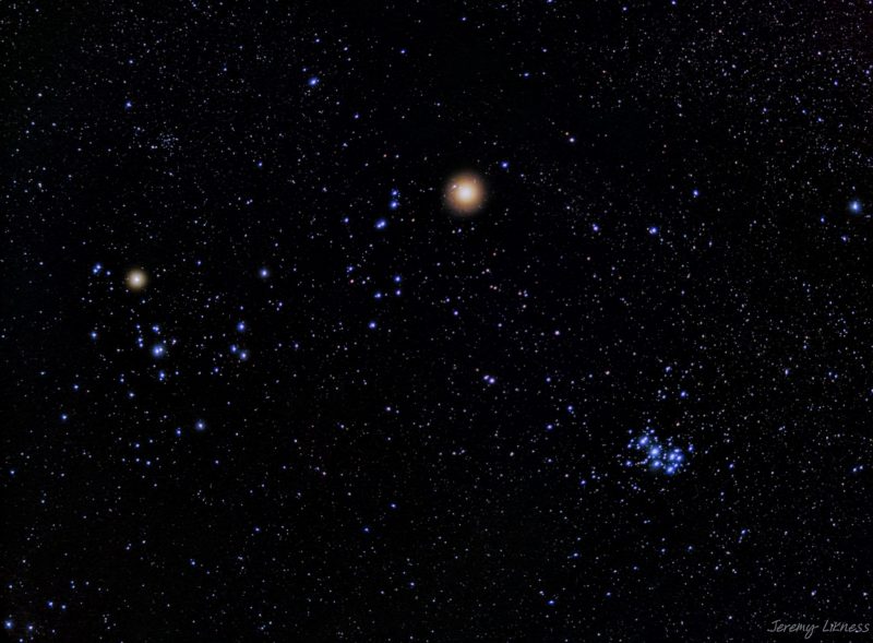 A multitude of blue stars with 2 bright, reddish, star-like objects and 2 little bunches of blue stars.