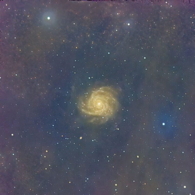 A bright yellow galaxy, a spiral seen head-on, in dusty, starry space.