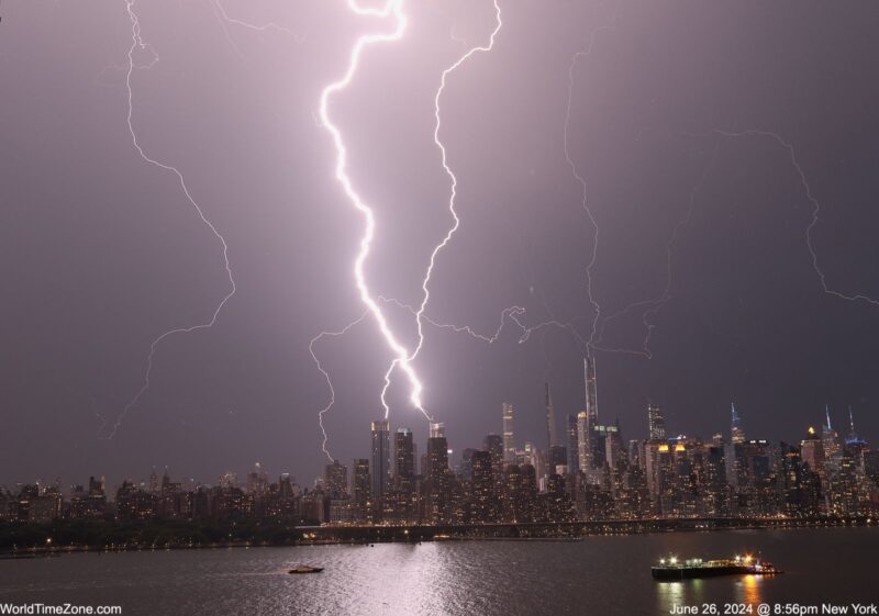 Lightning streaks from clouds to the Manhattan skyline, all reflected in a foreground body of water.