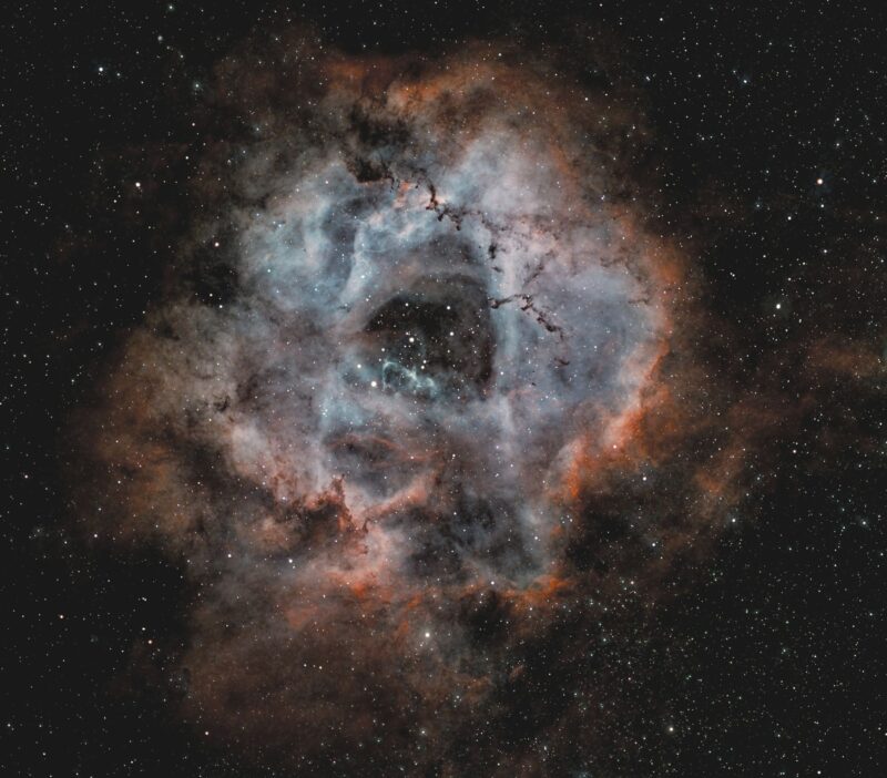 Large donut-shaped swirl of blue and green gas with thin dark lanes and numerous stars immersed within.