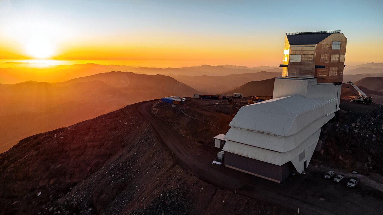 A white observatory on top of a brown mountain. There is alight glow in the sky.