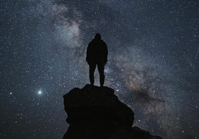 Intelligent life: Person standing on a large rock, silhouetted against a starry night sky.