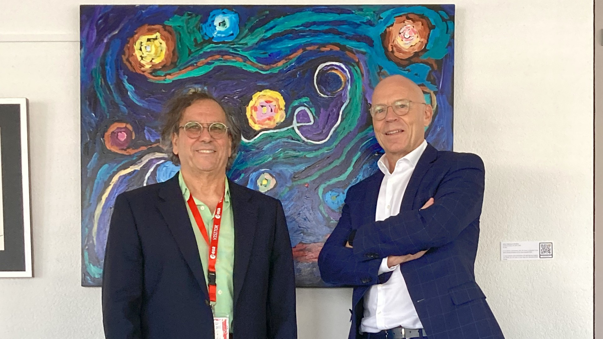 two men in sport coats in front of a colorful impressionist painting of planets