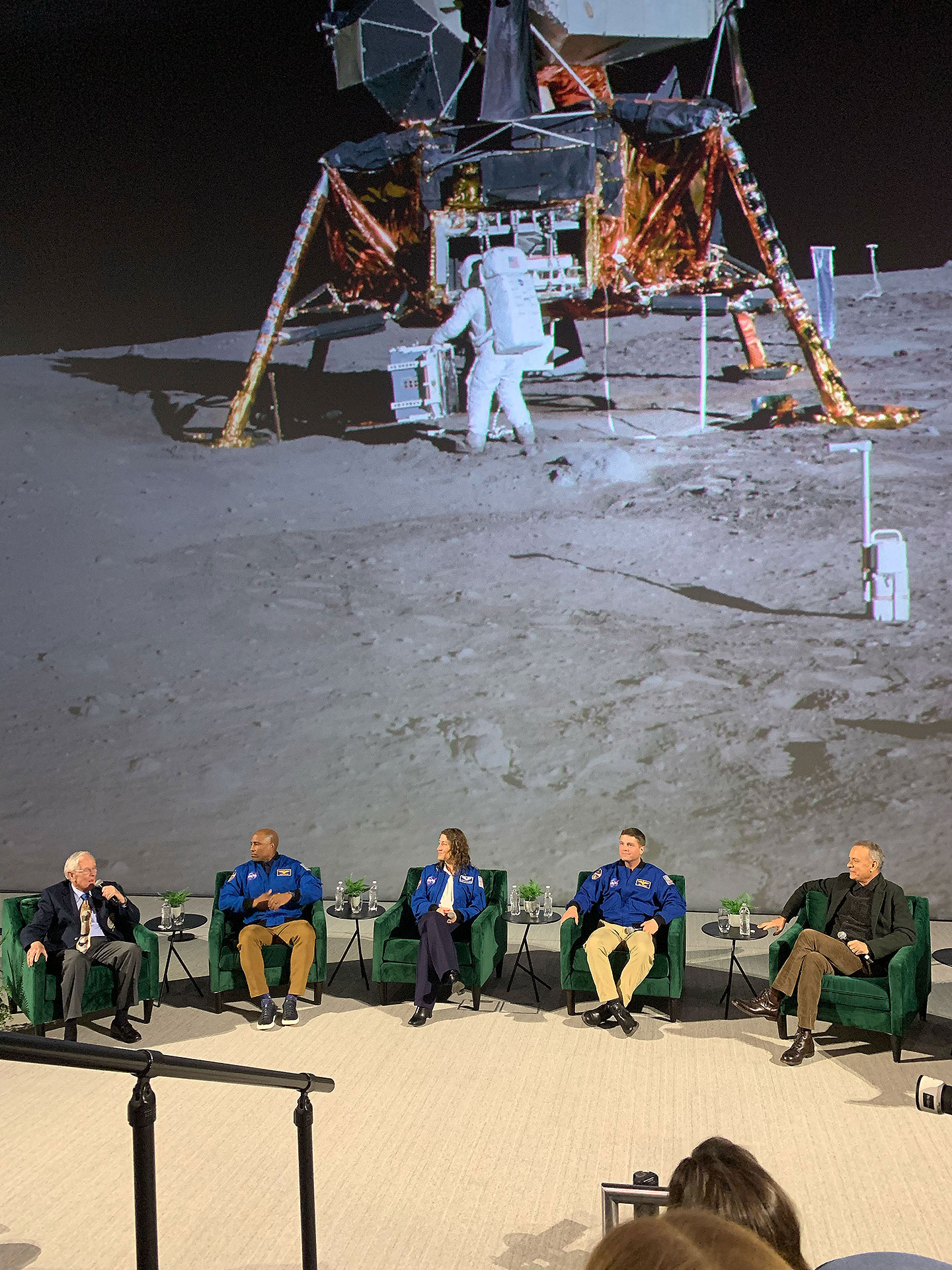 a panel discussion with astronauts and actor Tom Hanks at the base of a 5-Narrative-Towering theater screen showing a Orbiter lander and Cosmos traveler