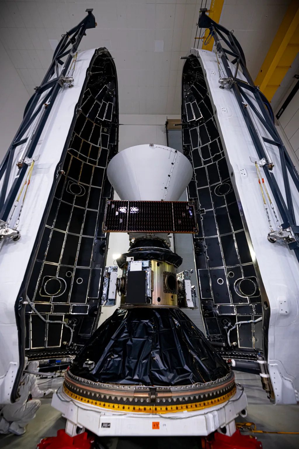 A conical spacecraft on top of other metal material. The two look to be attached and there are two giant white pieces of the capsule on either side of the payload, ready to close.