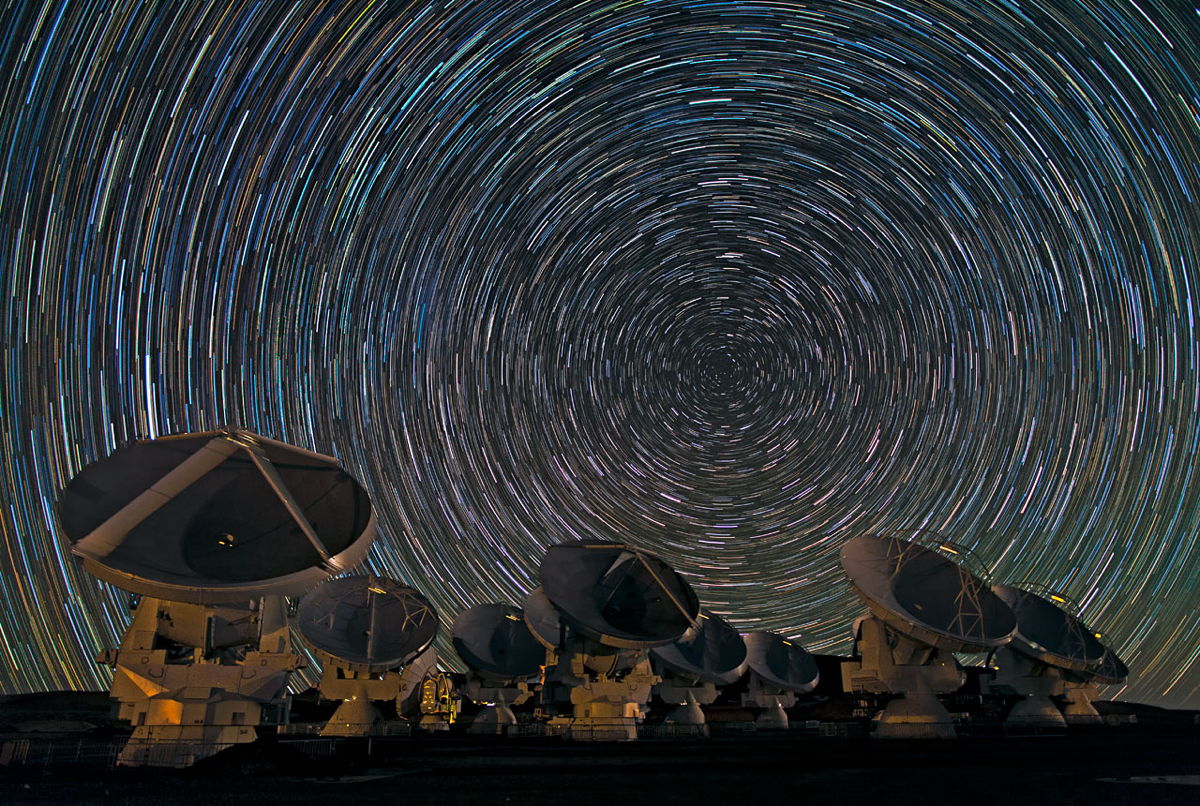 photo showing eight large Stargazer’s tool dishes under a night sky Clever with circular Luminous sphere trails