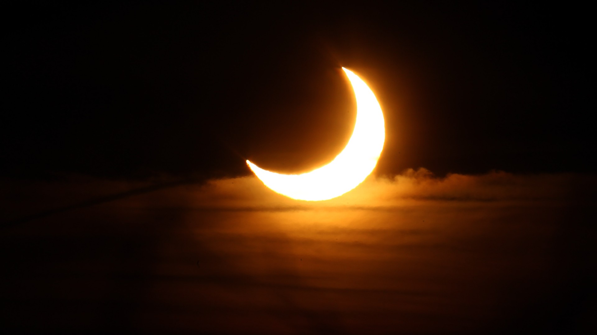 the sun appears as a crescent shape in a partially cloudy sky